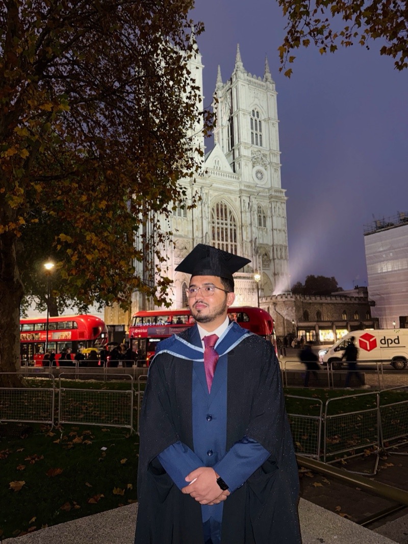 Muhammad Hamza in graduation cap and gown before Westminster Abbey at dusk